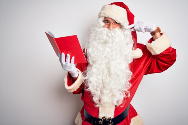 中年男子穿着圣诞老人的服装，在孤立的白色背景上读着书，微笑着，用手指、牙齿和嘴指着。牙齿健康的概念。图片下载