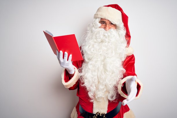 一位中年男子穿着圣诞老人的服装，在孤立的白色背景下读着书，微笑着友好地握手表示问候和欢迎。成功的事业。图片下载