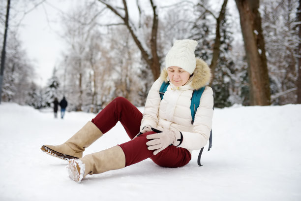 这是一个人在大雪纷飞的冬季公园里坠落的照片。女子在结冰的小路上滑倒了，伤了膝盖，坐在雪地里。图片下载
