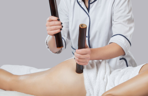 按摩师在美容院用竹竿按摩大腿、腿部和臀部。脂肪团和超重治疗。图片下载