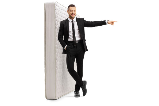 一个穿着黑色西装，心情愉快的年轻人站在一张床垫上，指着一边图片下载
