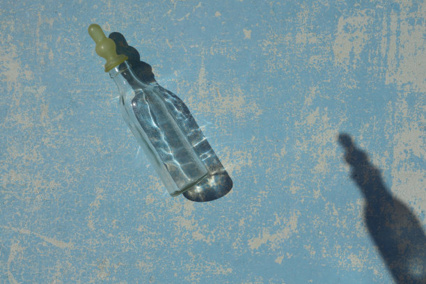 空的透明婴儿奶瓶喂养新生儿与阴影在蓝色柔和的颜色木质背景下，在自然的阳光下。平的。图片下载