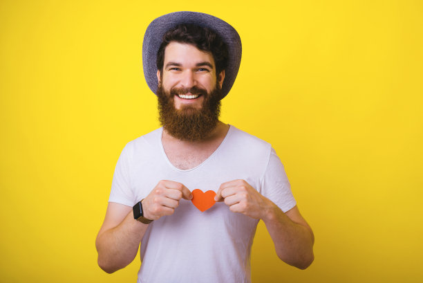 这张照片是一个留着胡子的男人，穿着白色t恤，手里拿着红色的心形纸图片下载