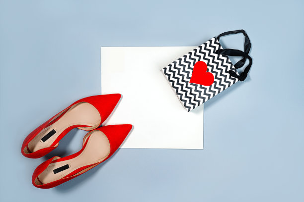 情人节概念与红色女人的鞋子和礼物袋与心在柔和的灰蓝色和白色的背景。图片下载