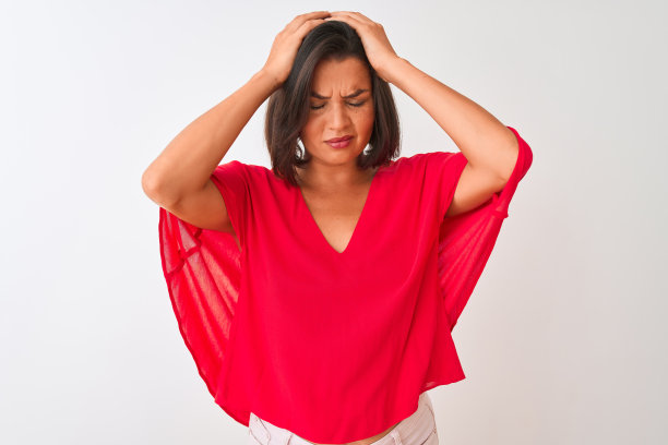 年轻漂亮的女人穿着红色的t恤站在孤立的白色背景遭受头痛绝望和压力，因为疼痛和偏头痛。手放在头上。图片下载