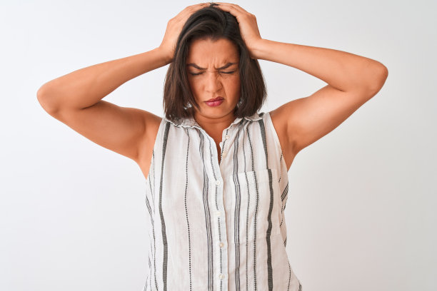 年轻美丽的女人穿着休闲条纹衬衫站在孤立的白色背景遭受头痛绝望和压力，因为疼痛和偏头痛。手放在头上。图片下载