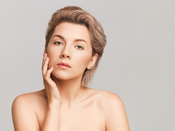 化妆在一个美丽的短发金发模特。在摄影棚里用灯光背景拍摄的。触及皮肤。为文本复制空间。图片下载