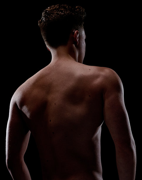 一个男人/一个人/腰部以上/后视图/ 20-29岁的成年英俊的人白人男性/年轻男子前面的黑色背景穿着半裙子谁是一个性感的象征/肌肉建设/赤膊图片下载
