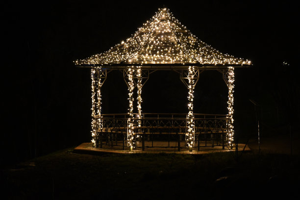 黑暗中传统灯光下的凉亭剪影。带有圣诞灯柱和屋顶的建筑凉亭。黑色背景上的新年庆祝装饰。图片下载