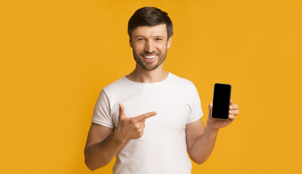 一名男子在黄色背景下展示智能手机黑屏微笑图片下载