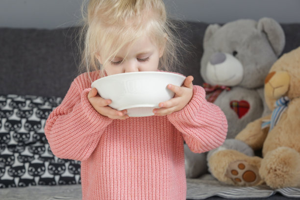 蹒跚学步的女孩从碗里吃东西，两岁的孩子自己吃东西图片下载