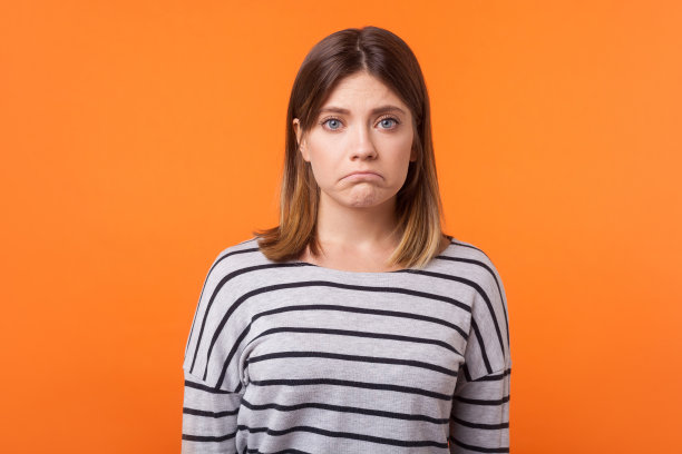 心烦意乱的年轻女子肖像与棕色头发在长袖条纹休闲衬衫。橙色背景隔离图片下载