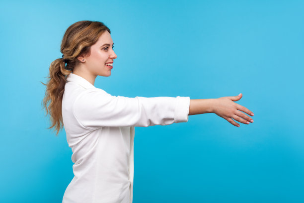 欢迎光临!友善好客的女商人握手的侧面图。蓝色背景图片下载