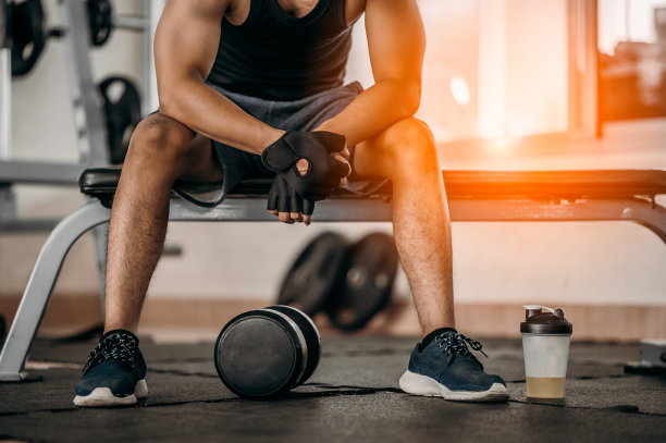 肌肉男在健身房里休息，坐在一瓶矿物盐和哑铃旁边。图片下载