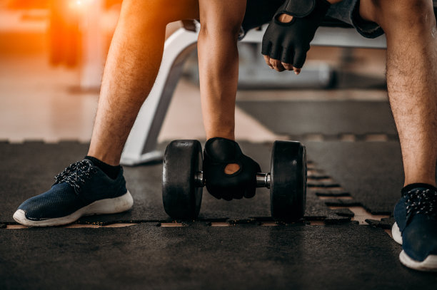 健美运动员在健身房用哑铃锻炼。健美运动员用哑铃锻炼。健身肌肉的身体图片下载