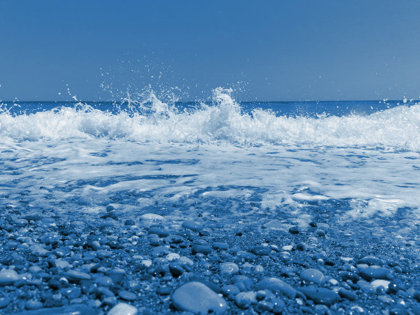 浅的多卵石海岸上的泡沫状波浪。2020年流行色调经典蓝色。图片下载