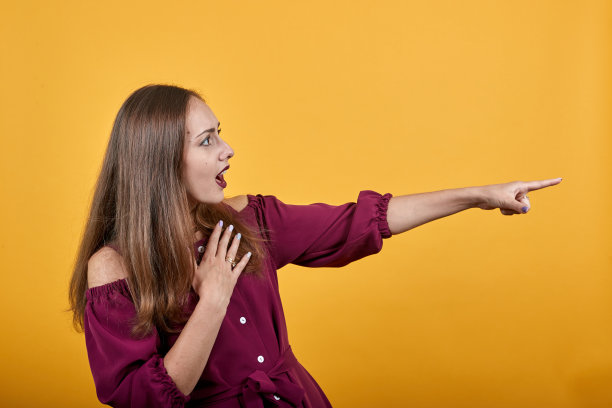 女士在勃艮第衬衫在孤立的橙色背景指向一边图片下载