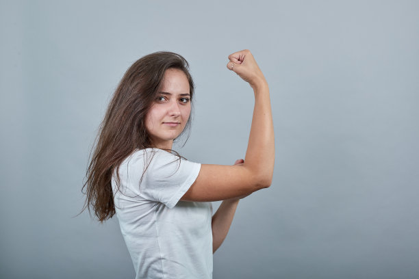 长头发的女人在孤立的灰色墙壁前做着强有力的手势图片下载