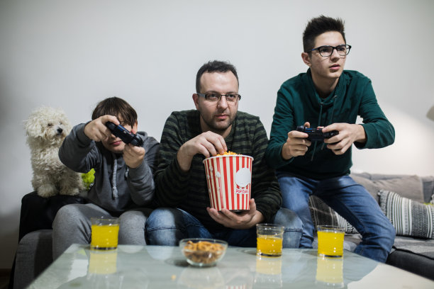 叔叔和他的两个侄子一起玩电子游戏。也可能是父子关系。图片下载