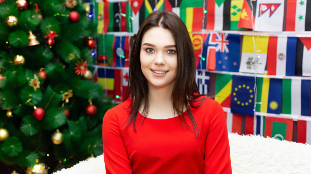 一个穿红衣服的女孩坐在圣诞树旁。图片下载