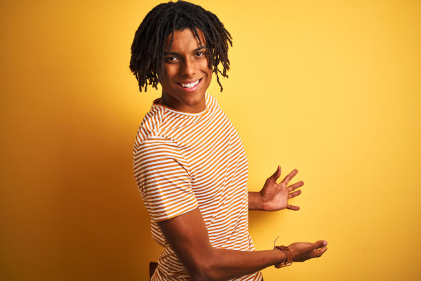 一个黑人，梳着雷鬼辫，穿着条纹t恤，站在孤立的黄色背景上图片下载