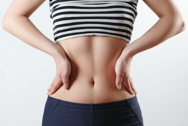 特写照片。一个身材修长的女孩穿着运动打底裤，一个主题展示了一个紧绷的身材和一个小肚子，双手放在腰部两侧的白色背景上图片下载