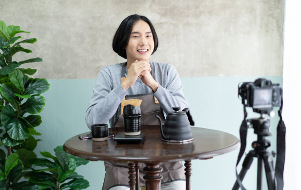 微笑的咖啡师亚洲人在围裙与记录摄像机拍摄和谈论视频拍摄与如何滴咖啡。创业小企业主的概念。制作博主或视频博主的概念。图片下载