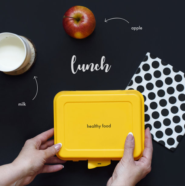 在黑暗的背景下，女孩拿着学校的午餐盒，牛奶和苹果。前视图。平的。健康饮食习惯概念。家庭食品的办公室概念。图片下载