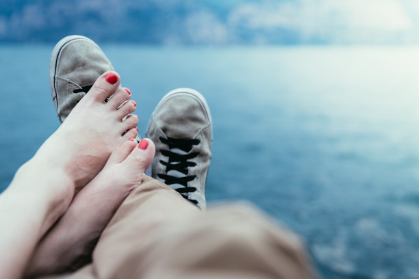 男孩和女孩正在享受他们的节日夜晚:运动鞋和赤脚的脚，湖和山素材图片