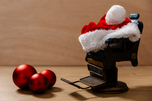有圣诞老人帽和三个圣诞树装饰球的收藏家的迷你光船椅子。木制背景。微距摄影图片下载
