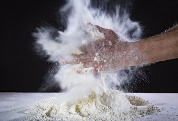 厨师的双手准备在桌上揉面，撒面粉。在面包店或家里用手揉面。面粉在空中飘浮。黑色背景。图片下载