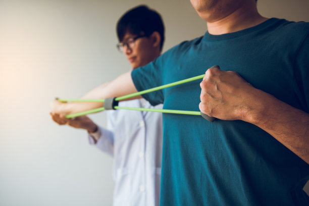 亚洲男性理疗师下降工作与病人做伸展运动与弹性运动带在医务室。图片下载