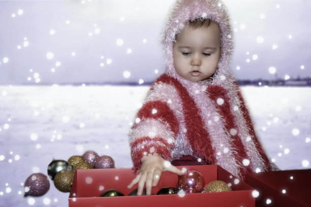 可爱的宝宝在冬天的雪地上玩圣诞球。穿条纹雨披的孩子。雪正在下降。圣诞节的概念，新年。图片下载