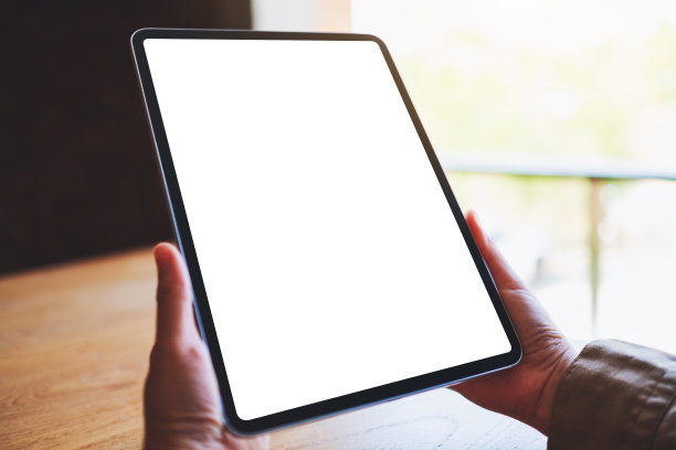 一个女人拿着黑色平板电脑和空白的白色屏幕在木桌上图片下载