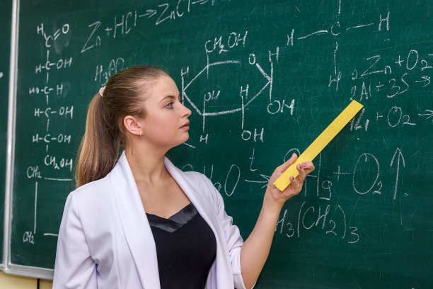 一个女人站在化学教室旁边，指着黑板图片下载