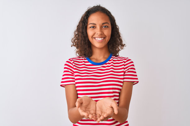 年轻的巴西女子穿着红色条纹t恤站在孤立的白色背景微笑与手掌在一起接受或给予手势。保存和保护图片下载