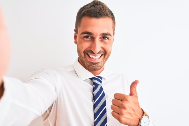 年轻英俊的商人在孤立的背景下用智能手机自拍，开心地笑着做ok手势，竖起大拇指，很棒的手势图片下载