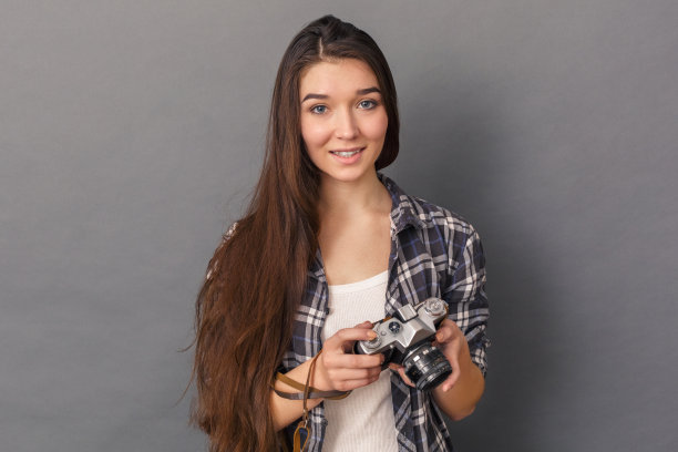 摄影的爱好。年轻女子站在工作室孤立的灰色与胶片相机微笑好奇图片下载