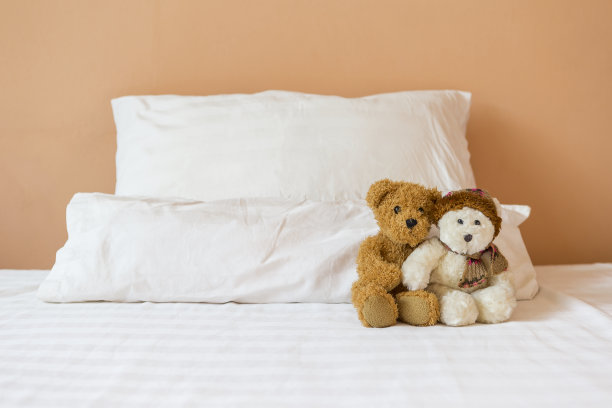 棕色和白色的小泰迪熊一起坐在床上，枕头放在橙色的墙上图片下载