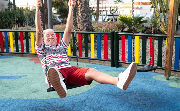 在秋千上玩得很开心。一位迷人的白发老人在公园里和孩子们一起玩游戏图片下载