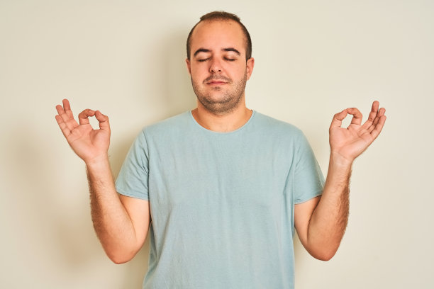 年轻男子穿着蓝色休闲t恤站在孤立的白色背景放松和微笑，闭上眼睛做冥想手势与手指。瑜伽的概念。图片下载