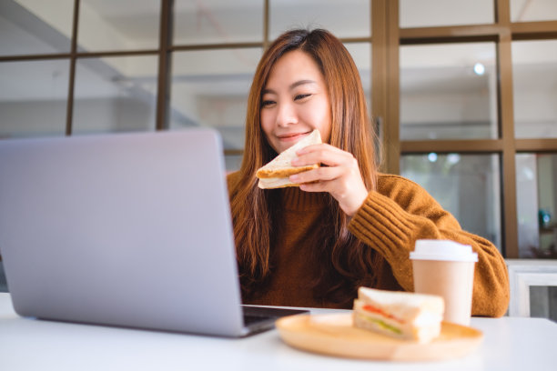 女人拿着全麦三明治吃着，同时在电脑上工作图片下载