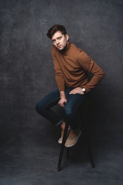 英俊随意的男人坐在椅子附近的一堵深灰色的墙，看向一边，肖像图片。图片下载