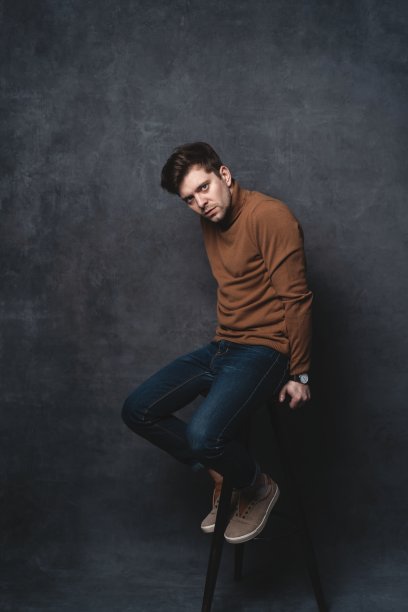 英俊随意的男人坐在椅子附近的一堵深灰色的墙，看向一边，肖像图片。图片下载
