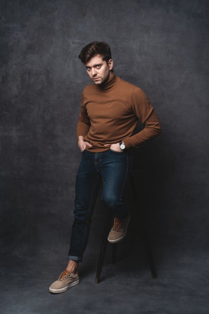 英俊随意的男人坐在椅子附近的一堵深灰色的墙，看向一边，肖像图片。图片下载