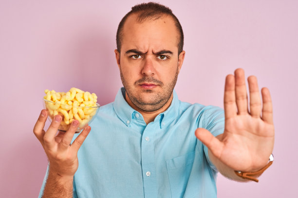 一个年轻人拿着碗和挤压玉米站在孤立的粉红色背景与摊开的手做停止标志与严肃和自信的表情，防御手势图片下载