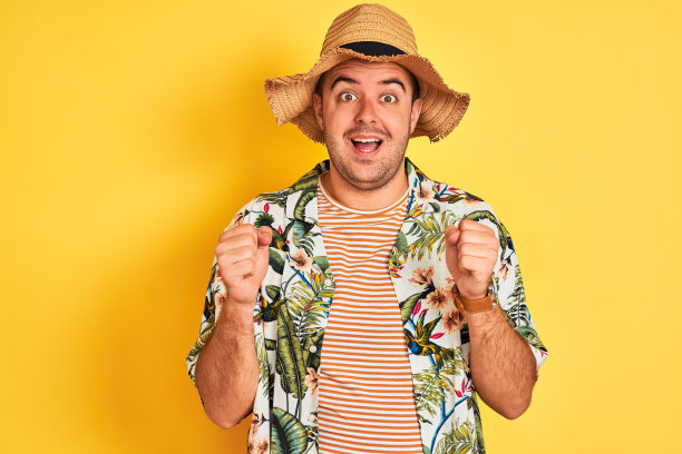 度假的年轻人穿着夏天的衬衫和帽子在孤立的黄色背景庆祝惊讶和惊讶的成功与手臂抬起和睁开眼睛。赢家的概念。图片下载