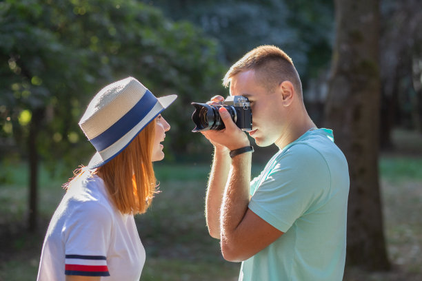 一对年轻的情侣在阳光明媚的夏日公园里拍下彼此的照片。图片下载