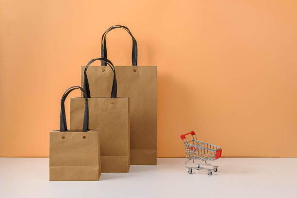纸购物袋和购物车或手推车在白色的桌子和柔和的橙色背景图片下载