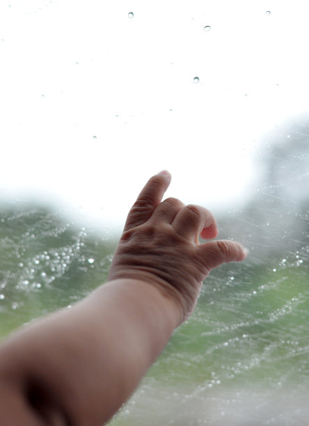 新生儿特写手。雨点落在玻璃窗上，以家在雨季抽象的背景，水滴落在玻璃上图片下载